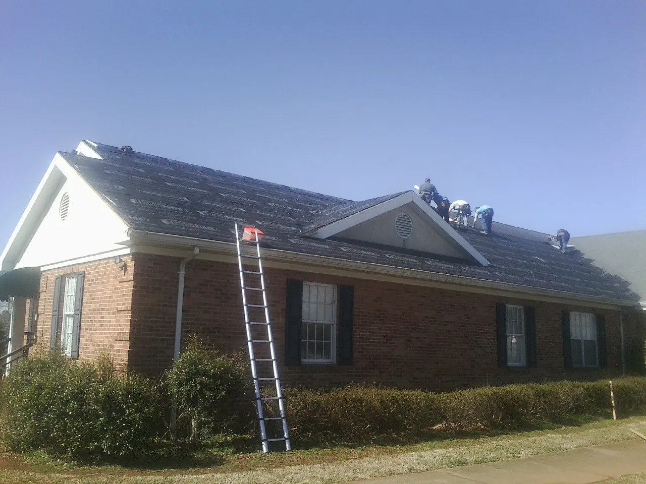 Crew tearing shingles off a brick ranch roof with a ladder set — Metal Roof Repair work by our crew in Kinards