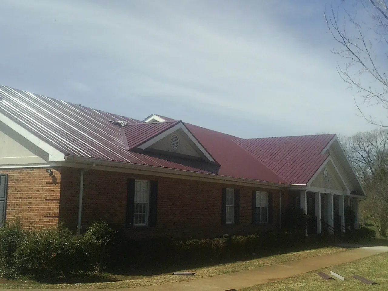 Red metal roof with gabled entries on a long brick building, from a Hail Damage Roof Repair job in Kinards