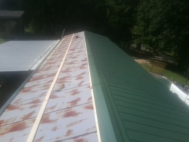 Old rusted panels beside newly installed green metal roofing — Wind Damage Roof Repair by Roofing Brothers in Kinards