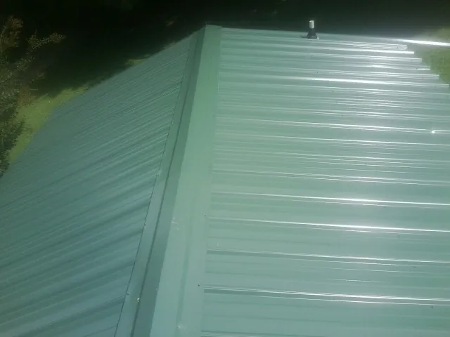 New green metal panels meeting at the ridge of a roof — Flat Roof Repair work by our crew in Kinards