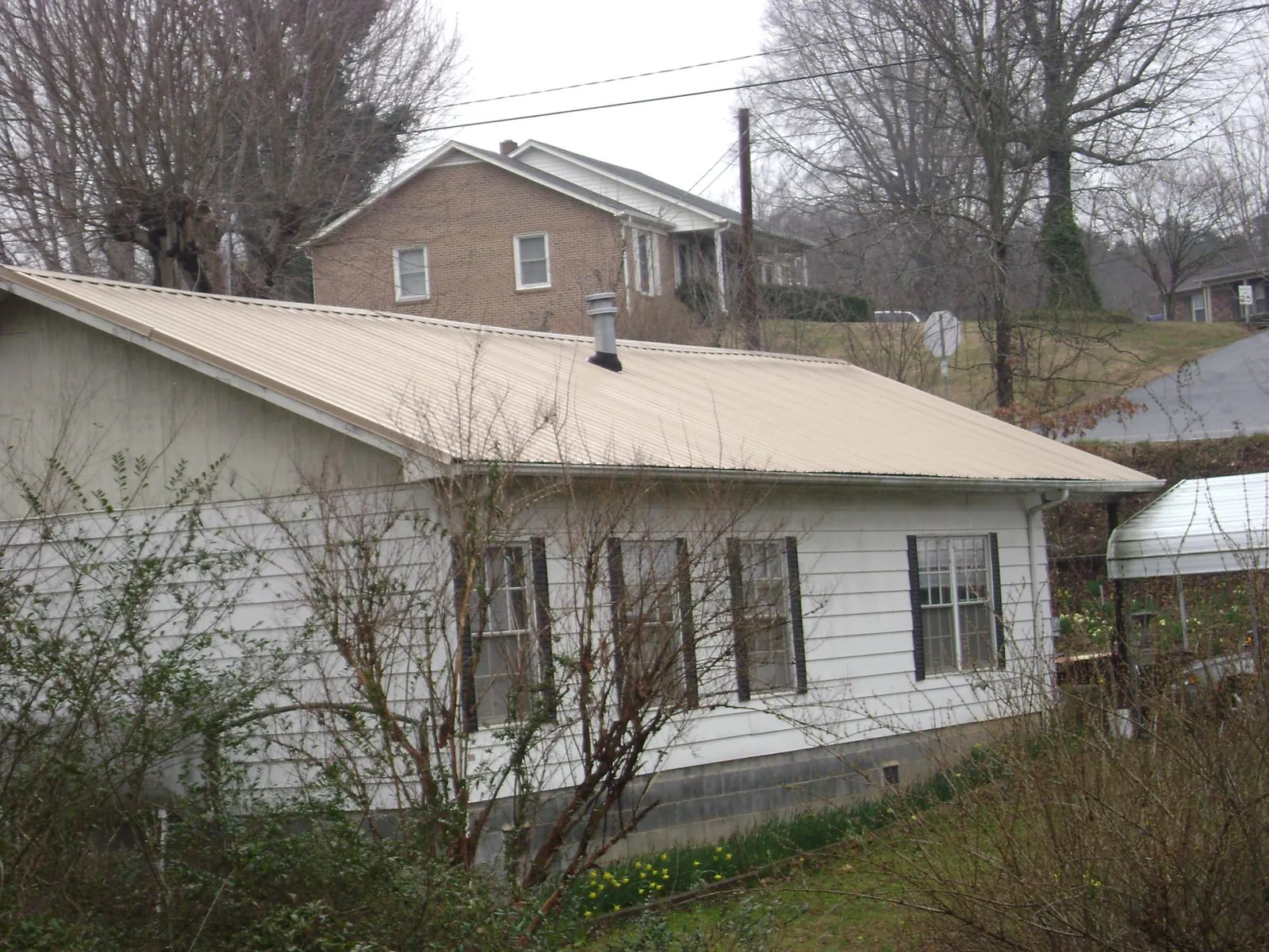 Tan metal roof on a white sided house set into a hillside — Commercial Roofing by Roofing Brothers in Kinards